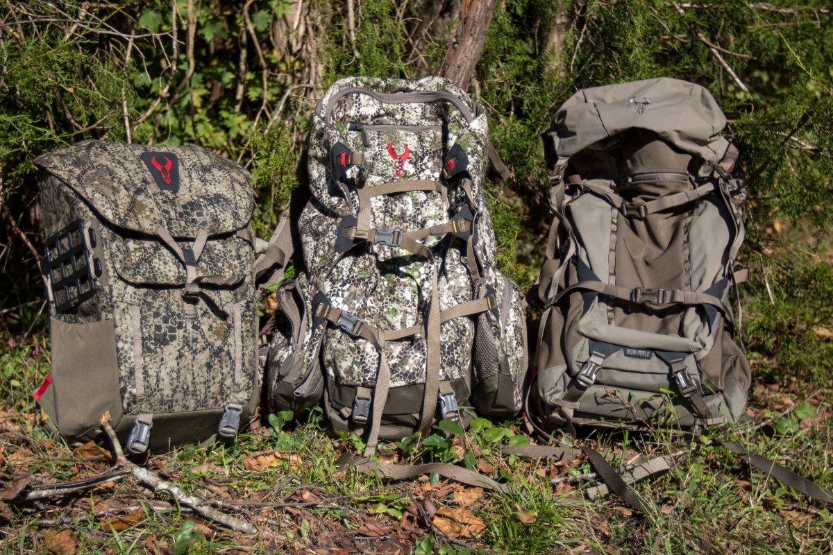 Three different sized hunting backpacks next to eachother in front of brush.