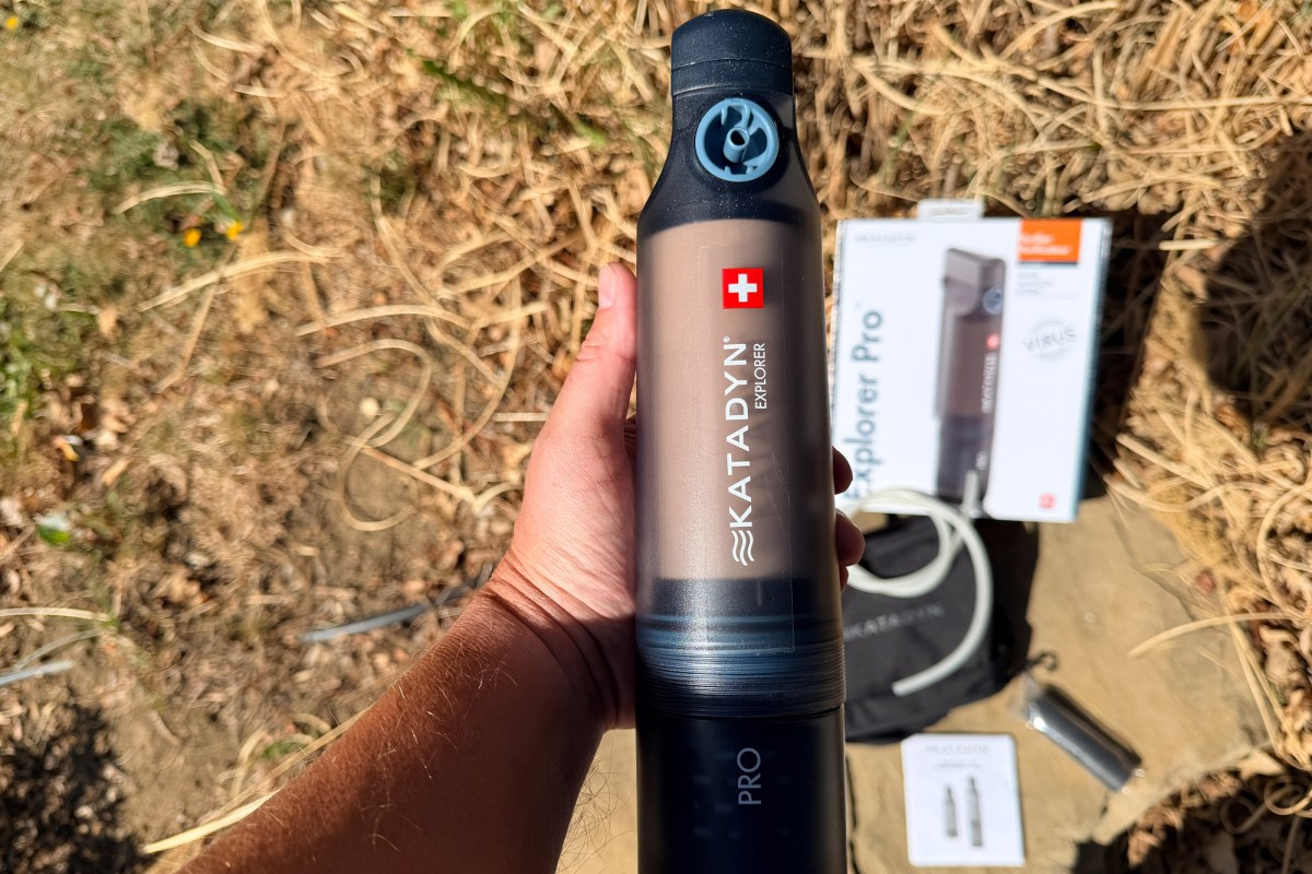 Hand holding the pump purifier with the box and accessories in the background