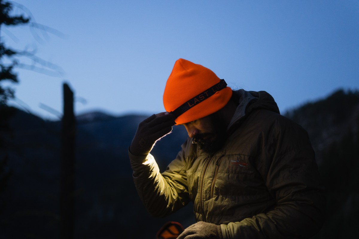 A person adjusts the Strike 1800 headlamp over an orange beanie at dusk
