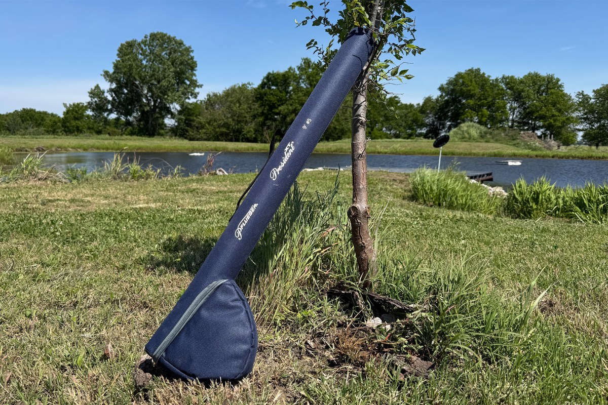 Pflueger President XT fly rod case leaning against a small tree near a pond