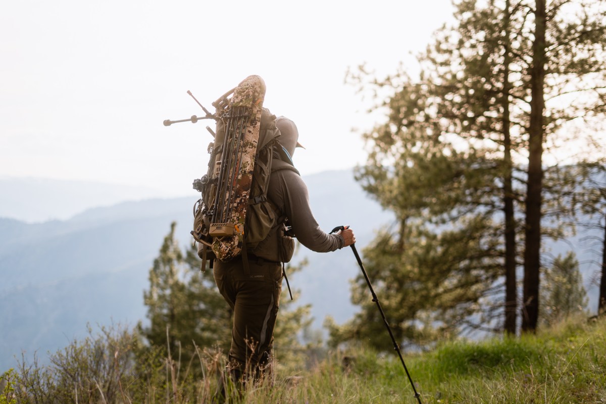 Backpacker carrying a packed NEMO Tensor sleeping pad on a mountain trail