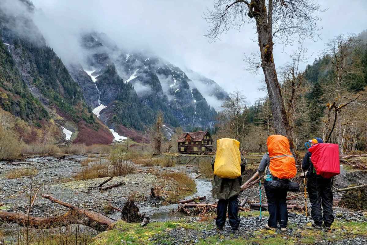 three hikers with rain covers on packs stand in mountainous valley