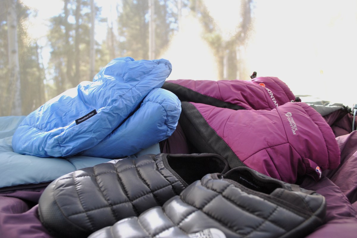 3 pairs of down booties, slippers, and socks scattered on top of a blanket inside a tent