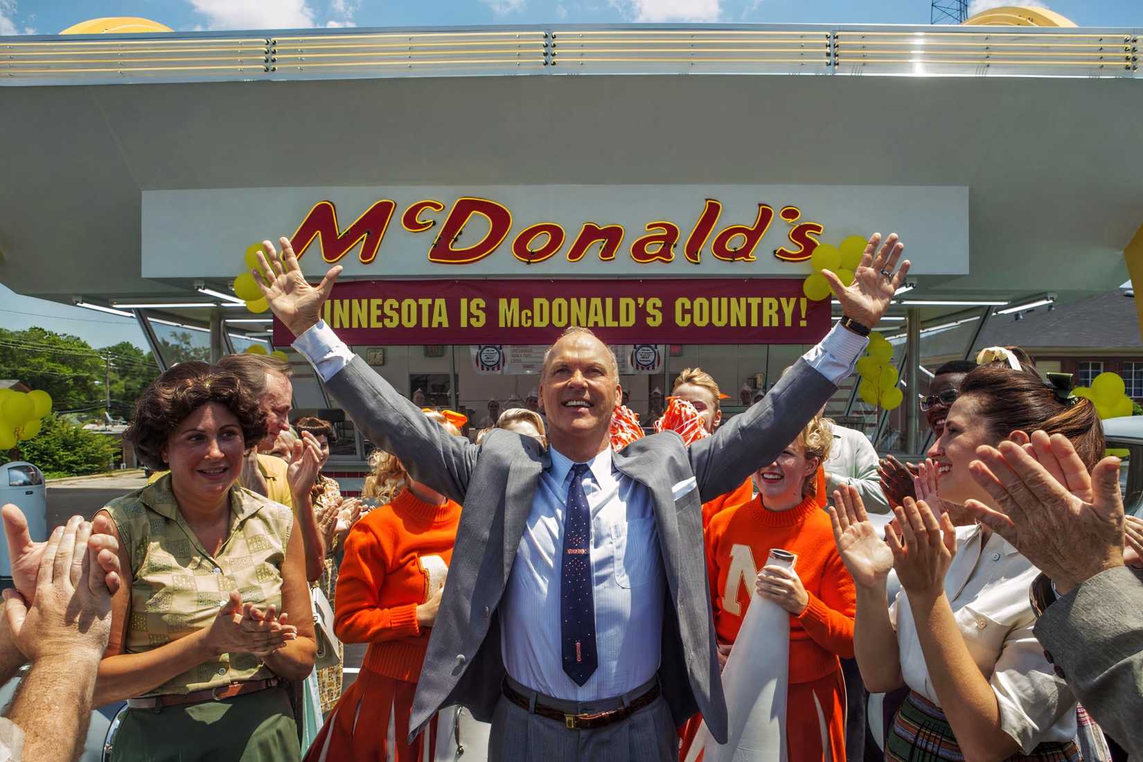 Ray Kroc stands with his arms raised outside a McDonald’s restaurant in The Founder.