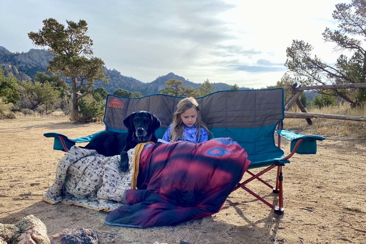 a young girl and a black lab dog with several camp blankets sitting on the Kelty couch
