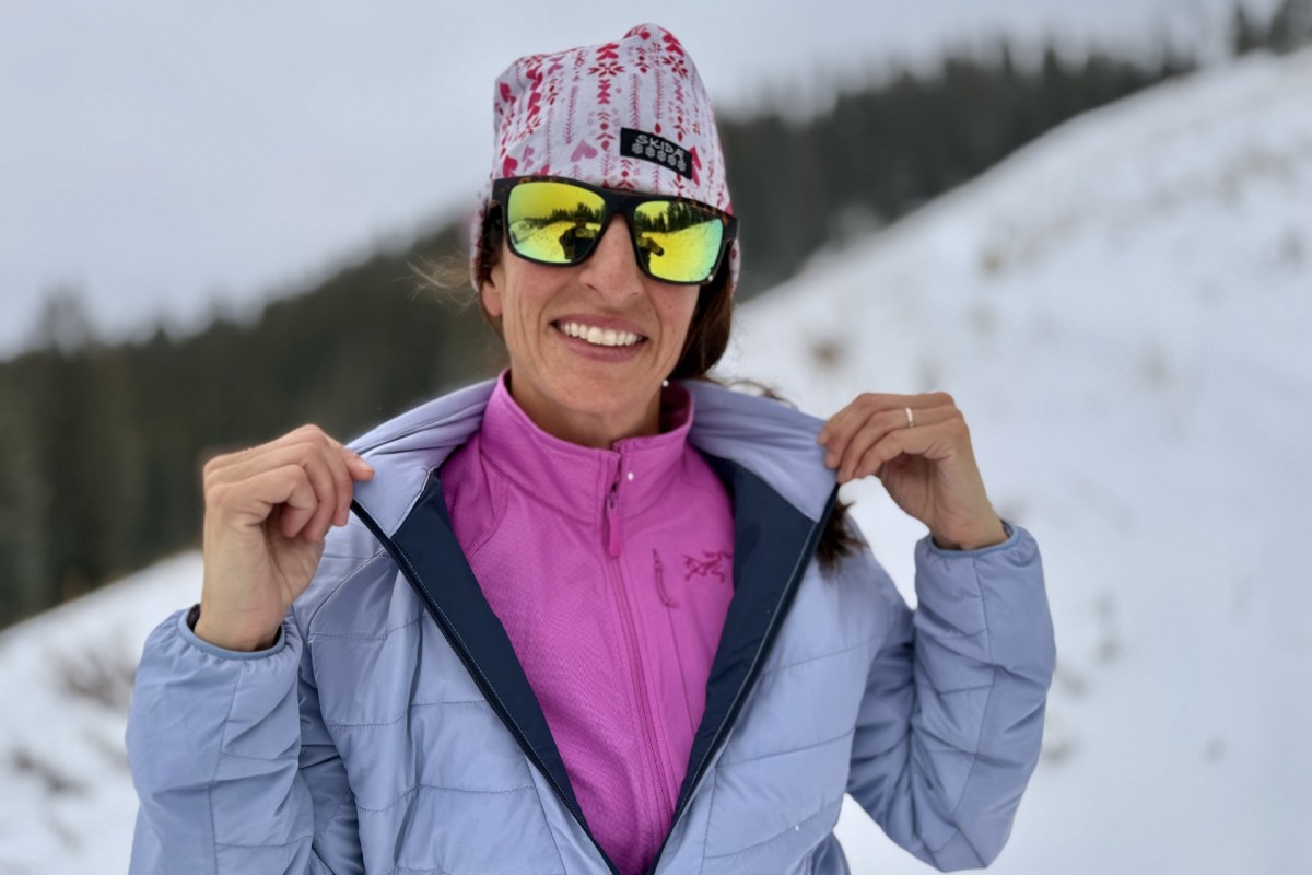 Woman showing the pink Arc’teryx Delta Jacket under a light blue winter jacket