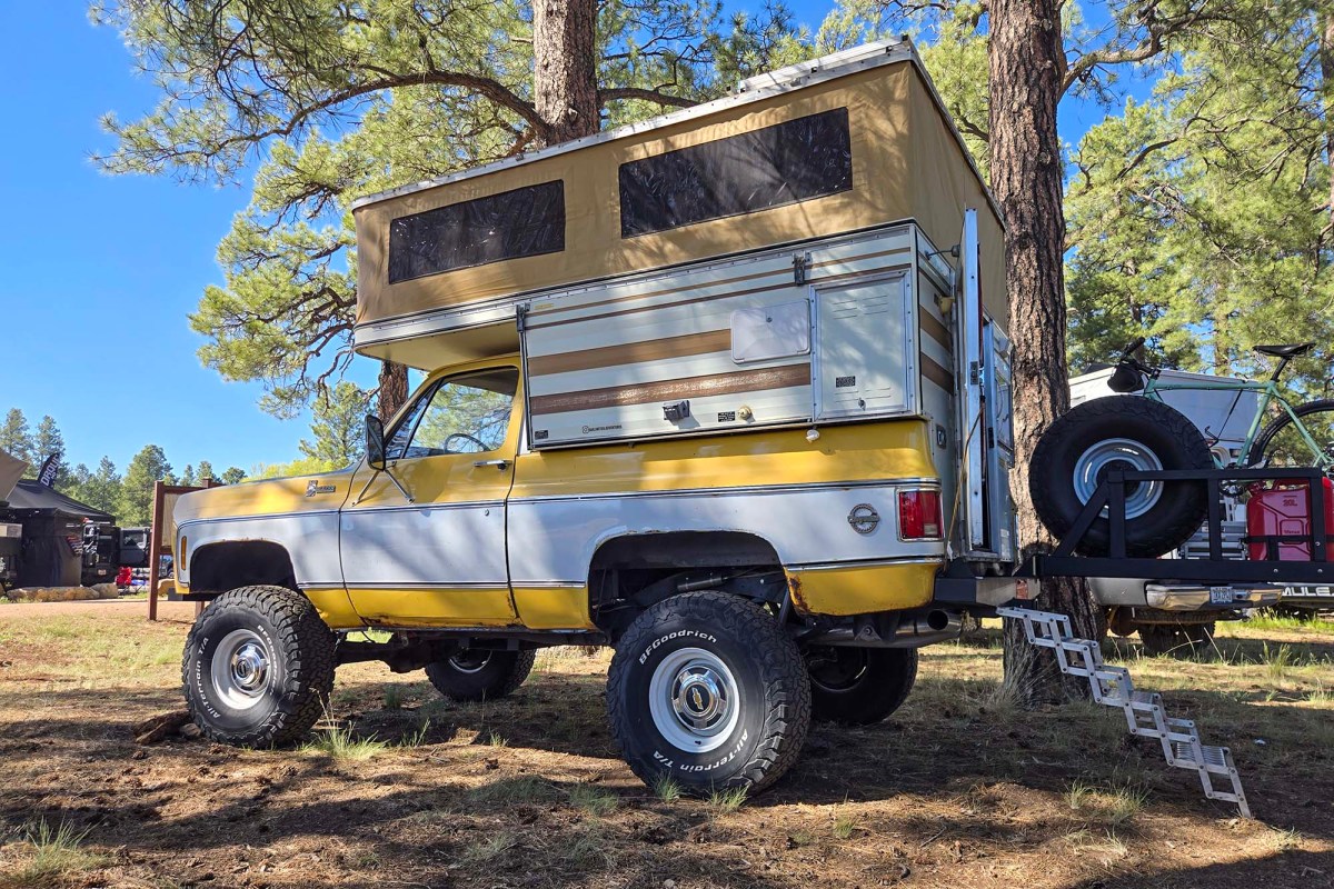 Yellow Chevrolet Blazer camper with a pop-up roof parked under pine trees