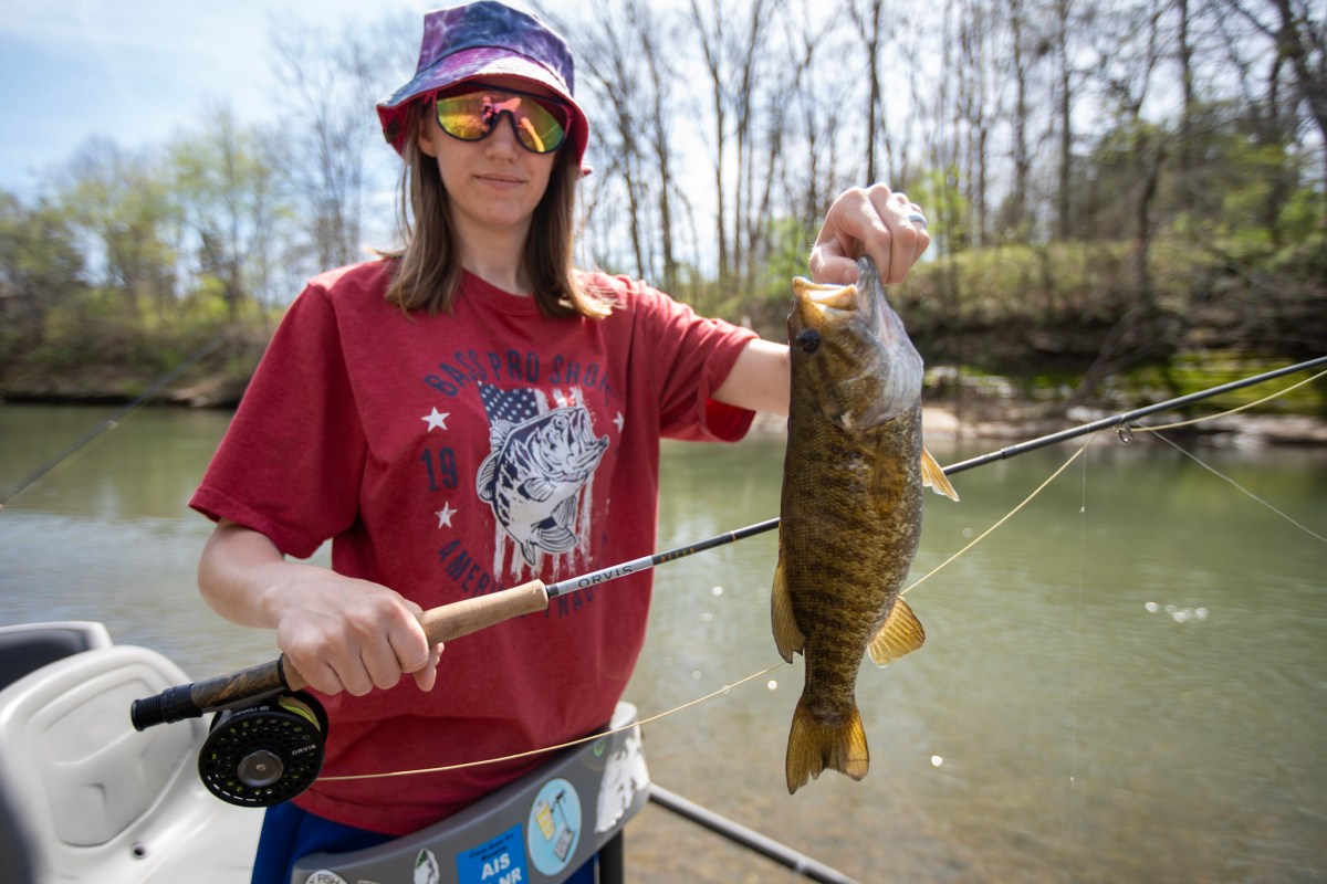 A woman holding a bass and a fly rod
