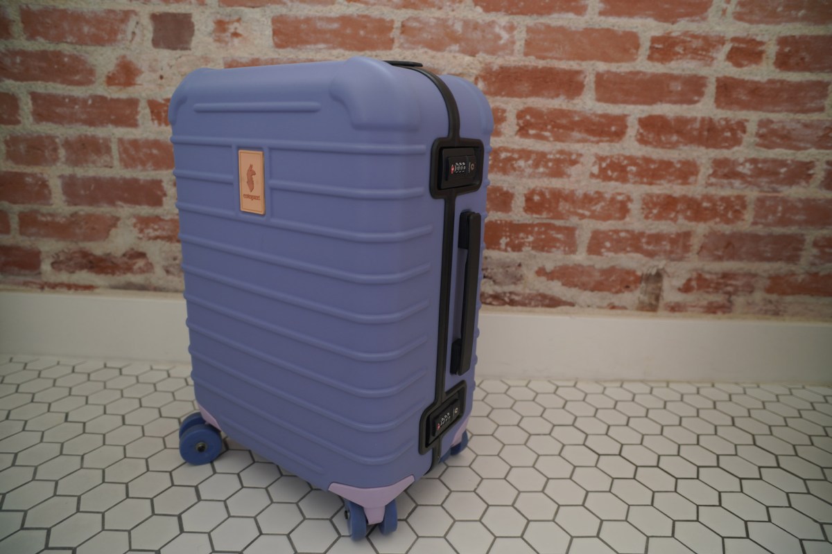 Coraza hard-sided carry-on luggage standing on a tile floor beside a brick wall
