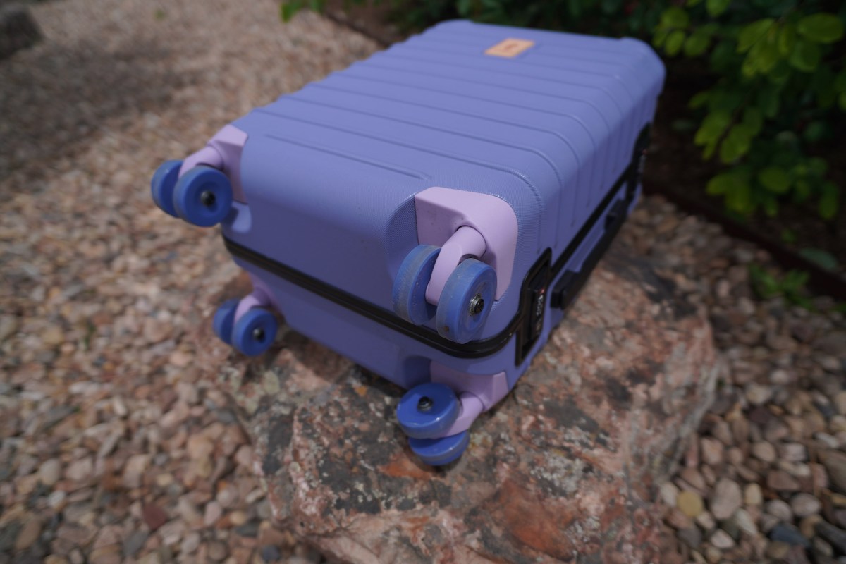 Close-up of the Cotopaxi Coraza Suitcase wheels and corner protectors on a rock