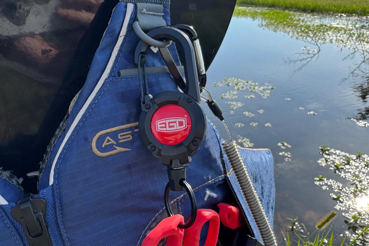An EGO multitool lanyard is clipped to a blue life vest, with red fishing tools tucked into the vest pocket beside the water