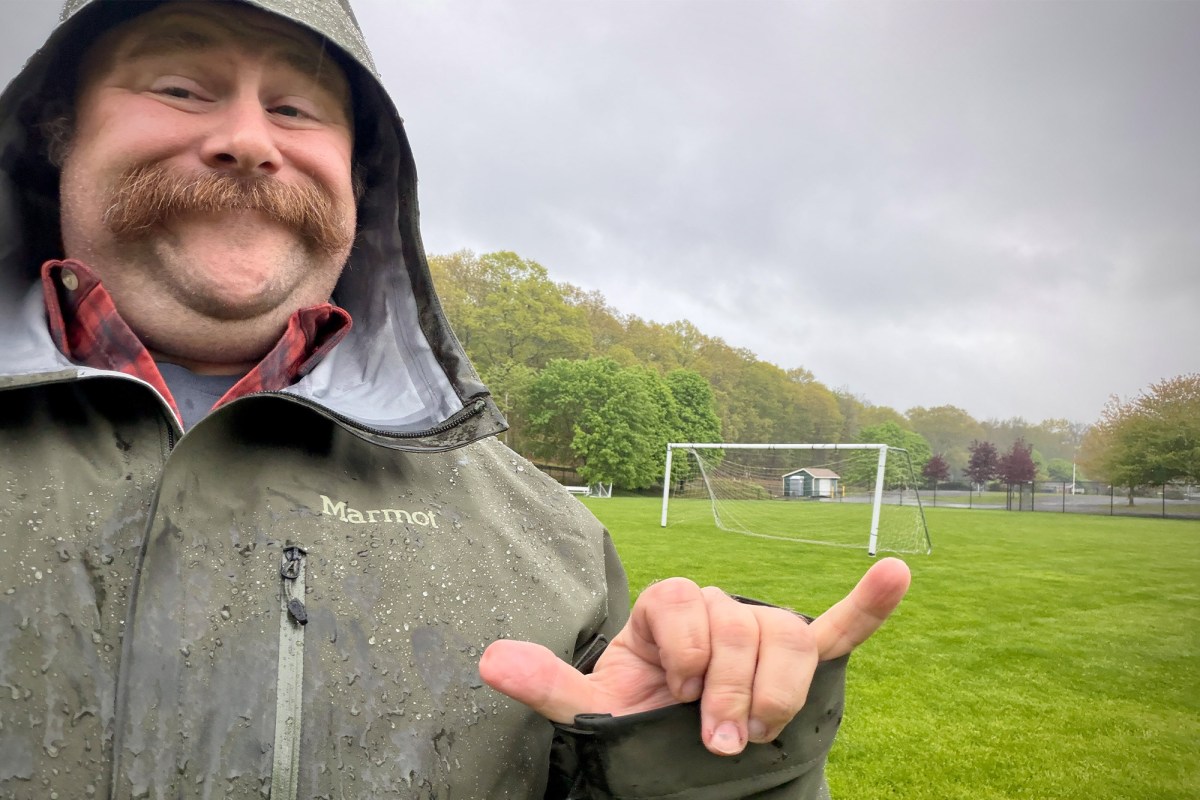 Person wearing the Marmot PreCip Evo Pro jacket in heavy rain near a soccer field