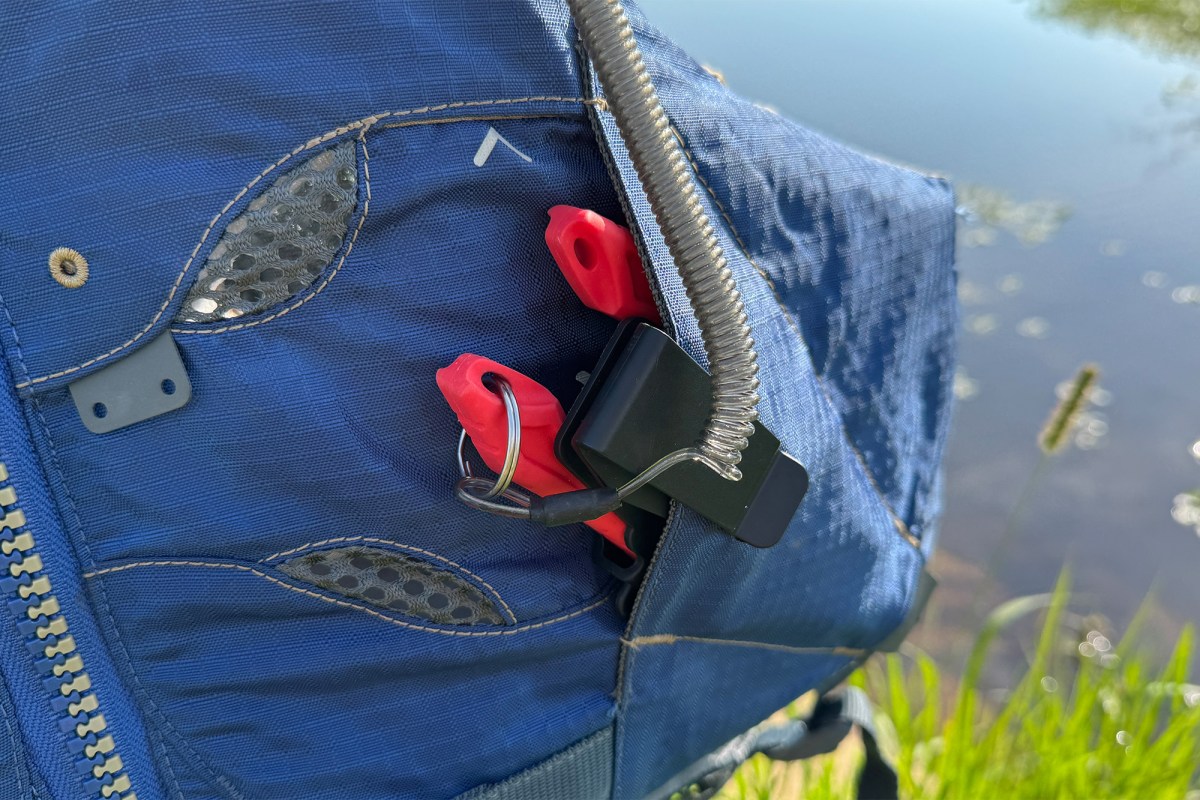 Red EGO fishing tools sit inside a blue life vest pocket, with a coiled lanyard clipped nearby at the edge of the water
