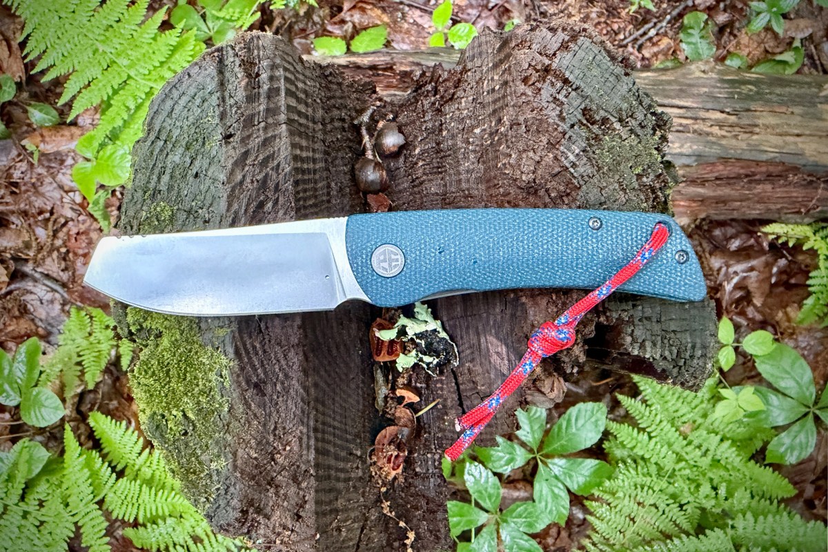 Open Flavorist knife with teal handle and red lanyard resting on a mossy tree stump