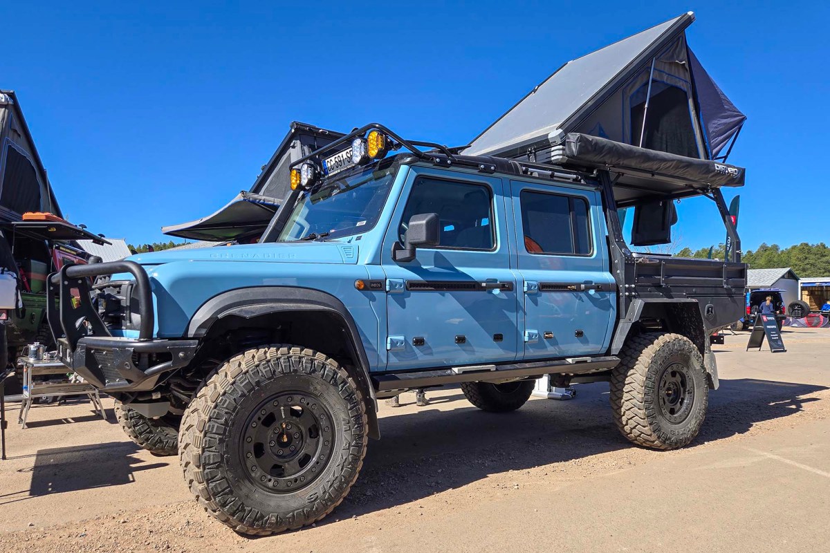 Blue INEOS Grenadier Quartermaster with off-road tires and a rooftop tent