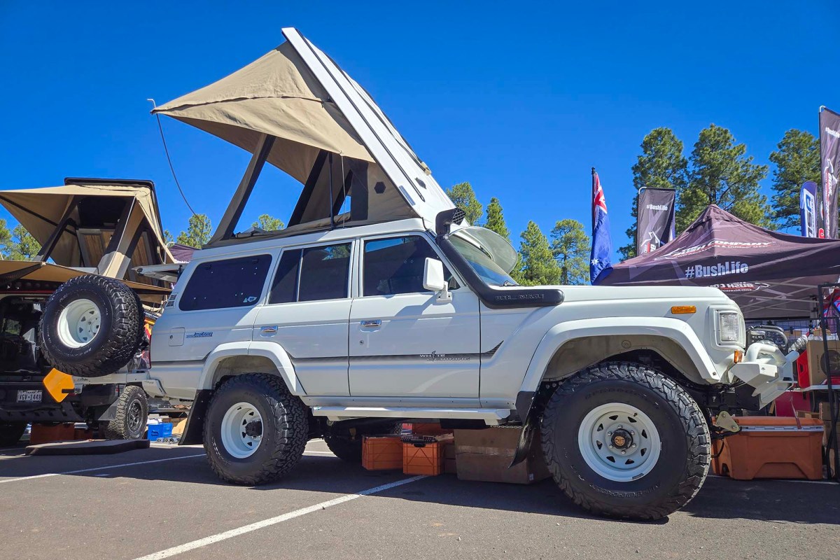 White Land Cruiser with a pop-up camper roof displayed at an outdoor event