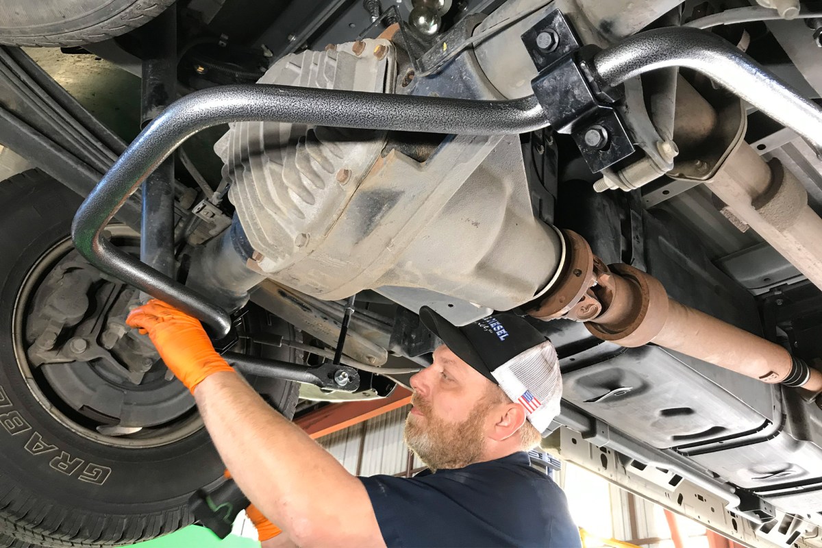 A rear anti-sway bar installed under a Ford vehicle while a mechanic works near the axle