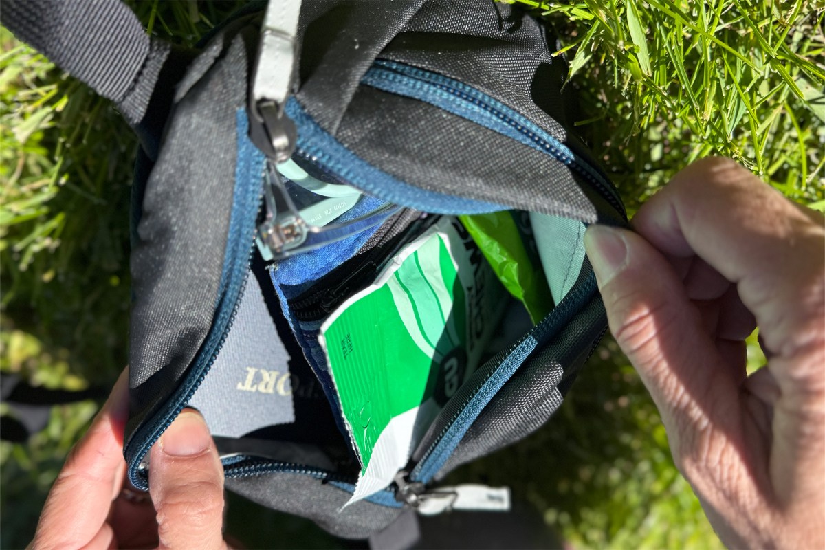 Open Arc’teryx waist pack showing a passport, snack, sunglasses, and small pouch inside