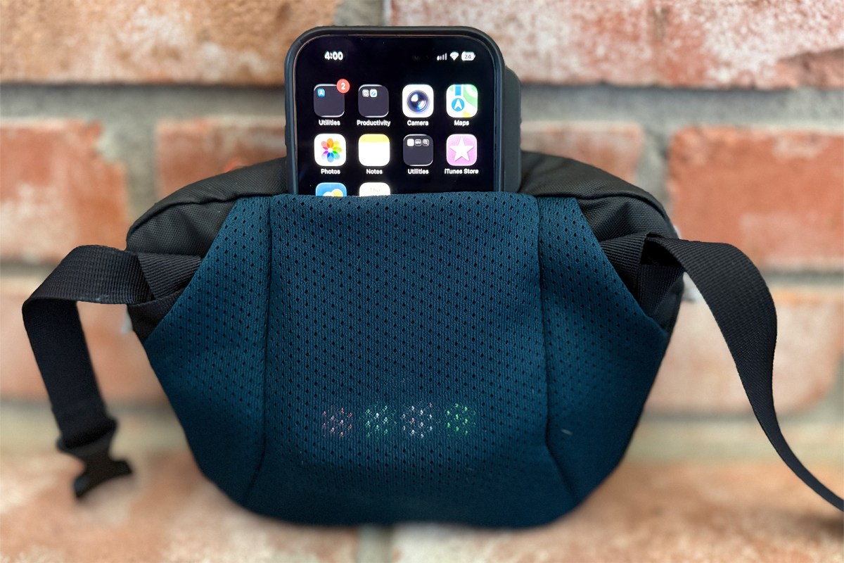 Phone tucked into the back sleeve of a black waist pack against a brick wall