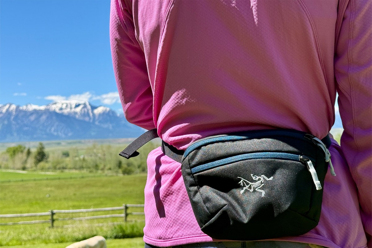 Close-up of a black Arc’teryx waist pack worn over a pink jacket with mountains behind it