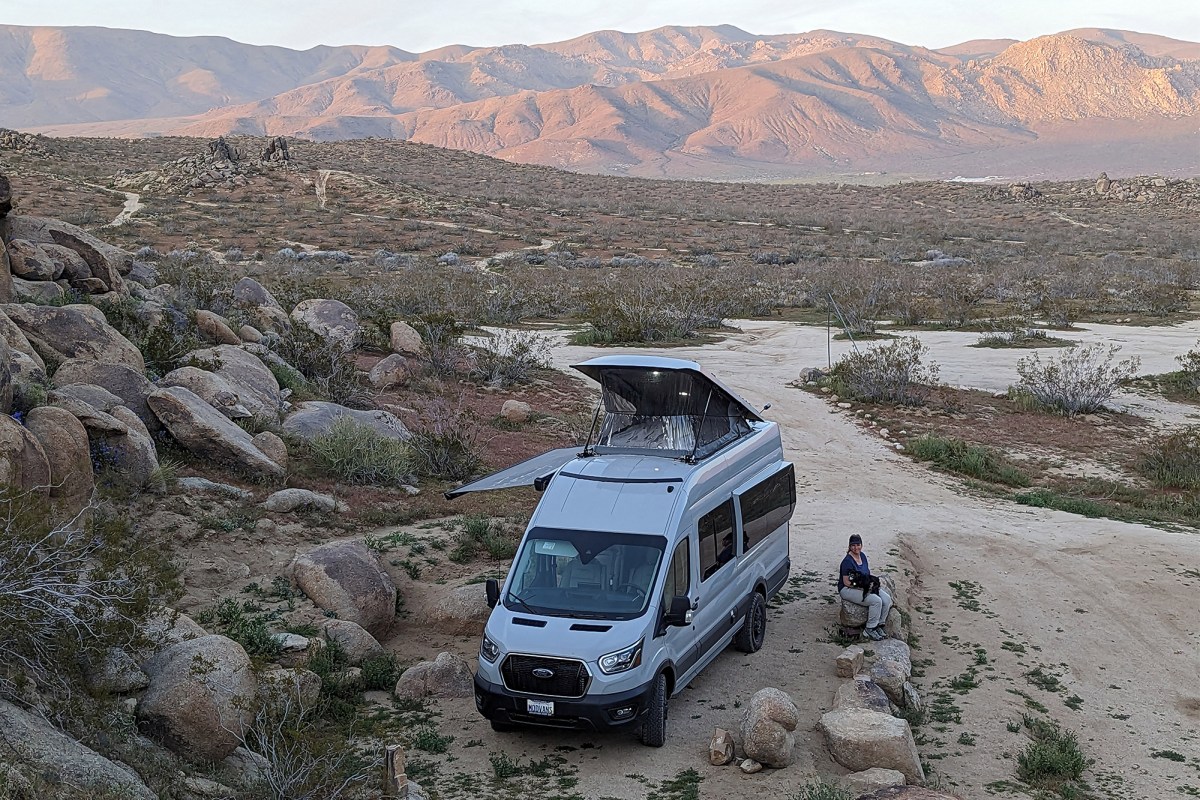 A camper van parked on a rocky desert road with mountains in the background