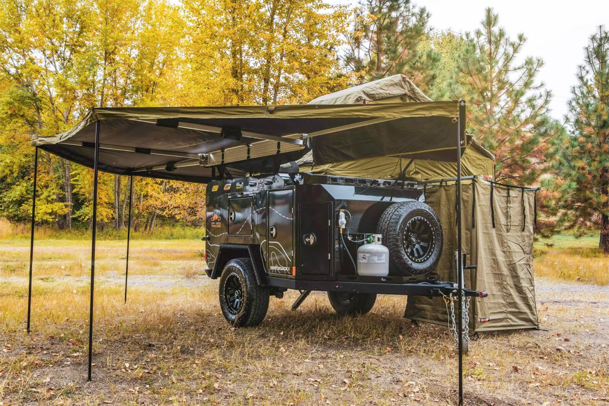 Off Grid Switchback trailer set up with a large awning and side room at a wooded campsite