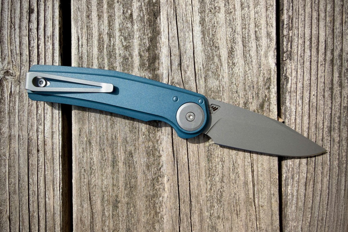 Open Work Sharp Madrone knife with a blue handle on weathered wooden boards