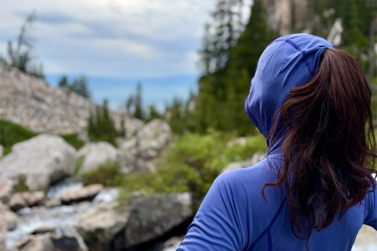 A hiker wears the Echo Hoodie with the hood up on a rocky trail