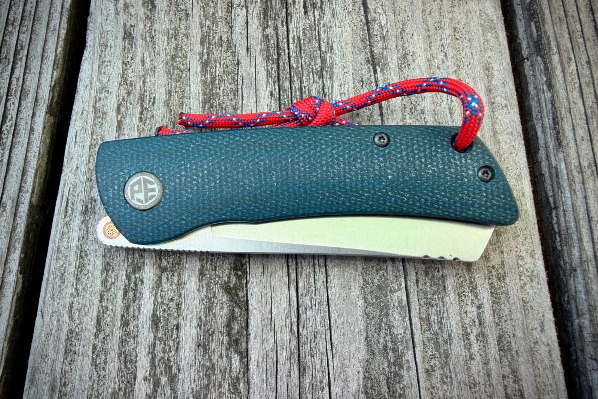Closed Flavorist knife with teal handle and red lanyard on weathered wood