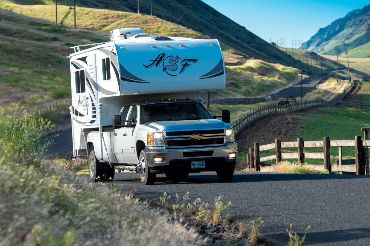 A pickup camper driving on a winding paved road through rolling hills