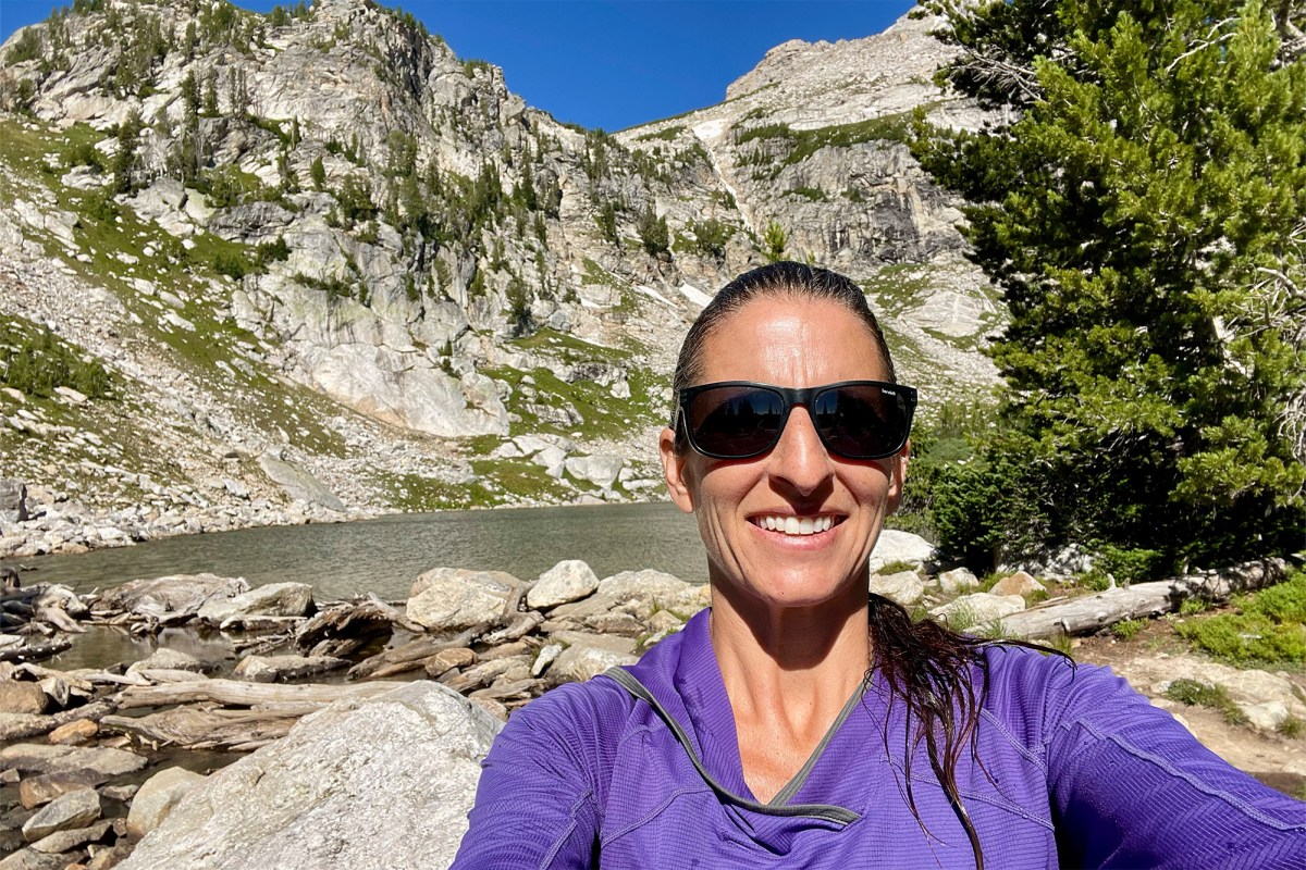 A hiker in a purple hoodie takes a selfie by a mountain lake