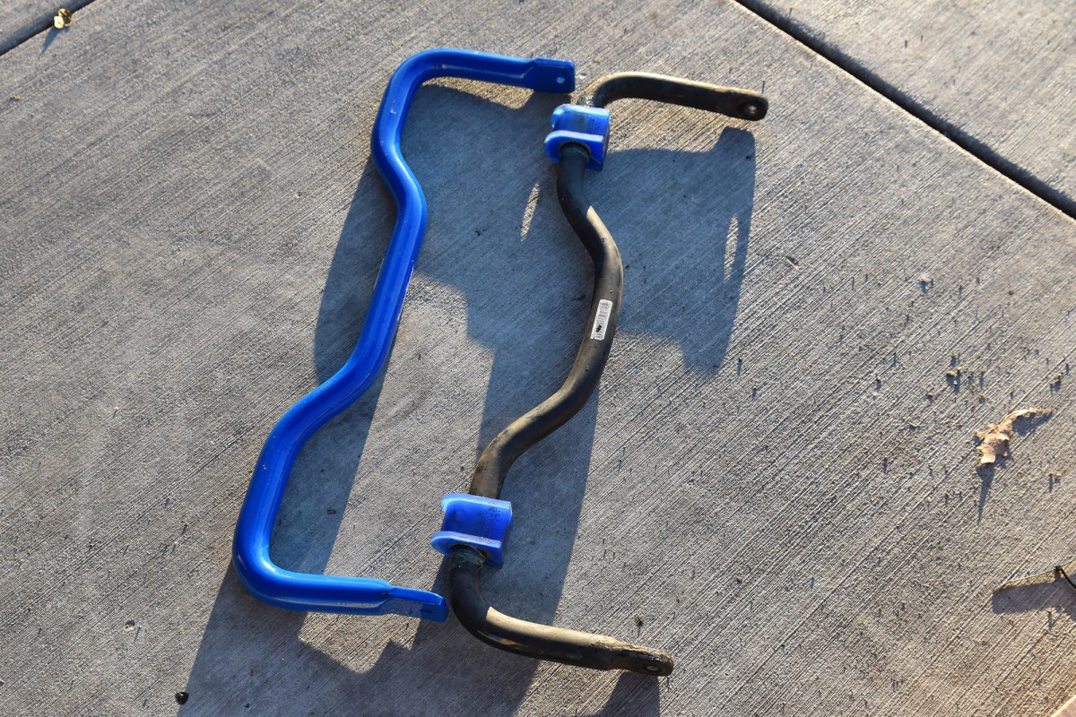 A blue SuperSteer sway bar shown beside the original black sway bar on concrete