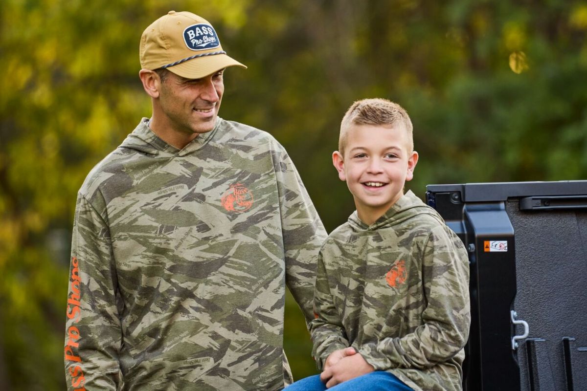 father and son in camo apparel sitting on truck bed