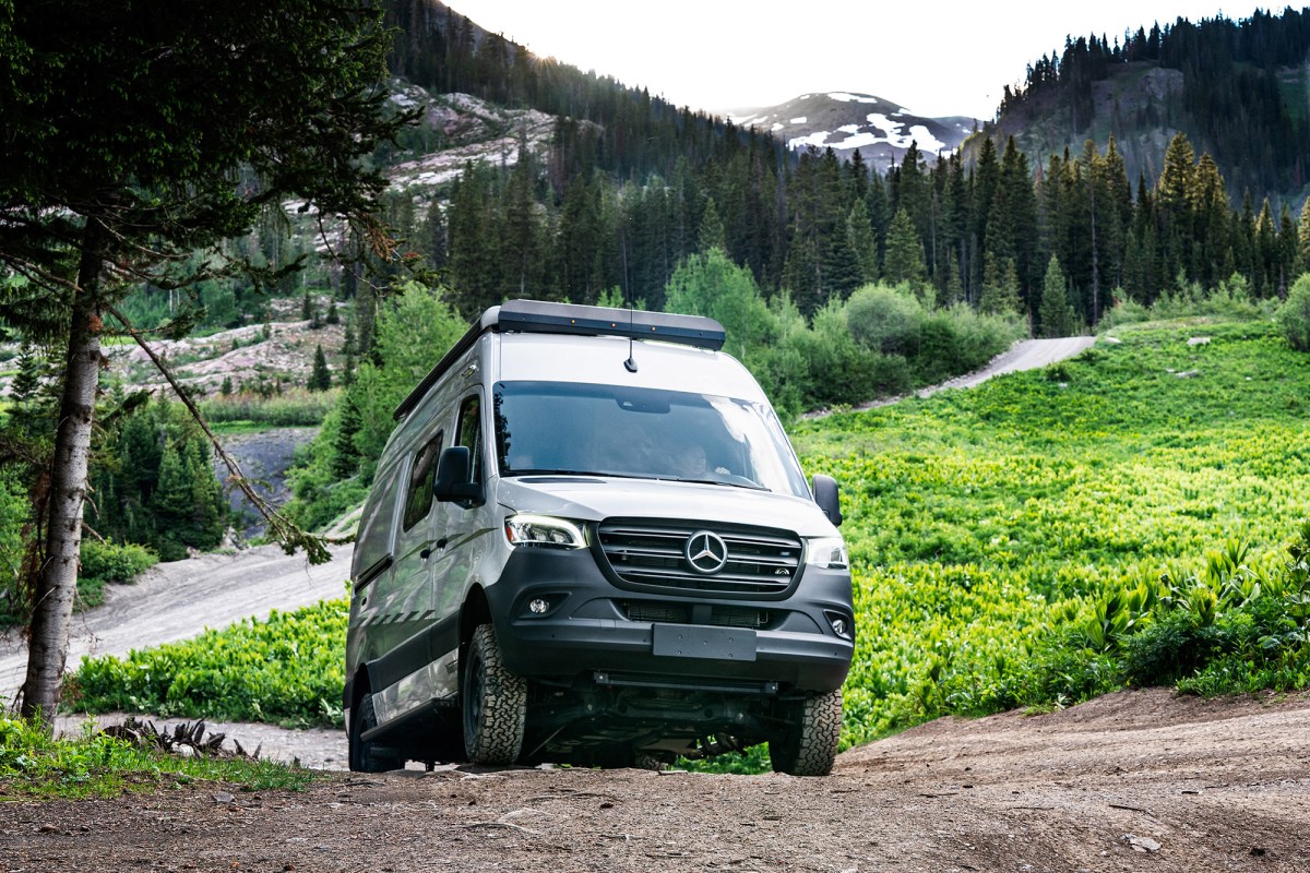 A Winnebago Revel van driving up a dirt incline in a green mountain area