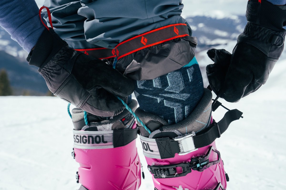 Close-up of skier tightening Rossignol AllTrack 130 Elite LV LT Ski Boots with gloves on in a snowy mountain setting