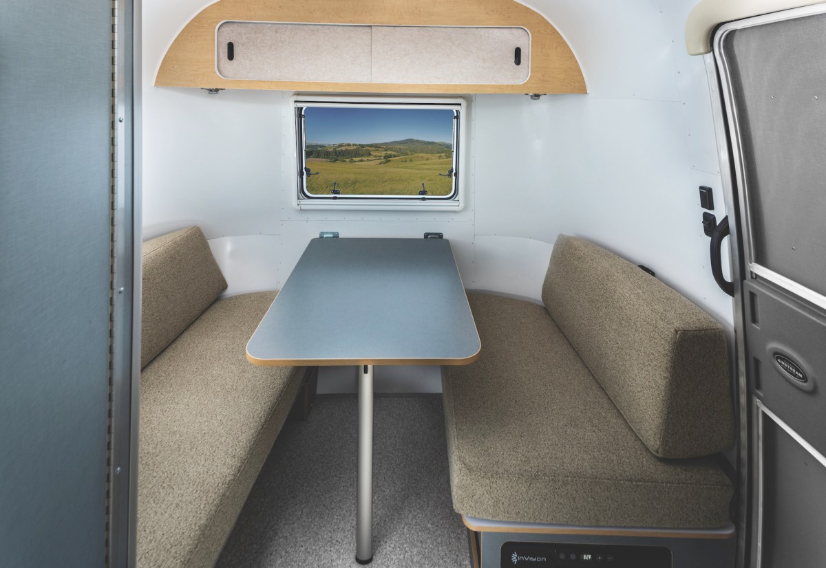 Two beige benches and a folding table inside an Airstream travel trailer.