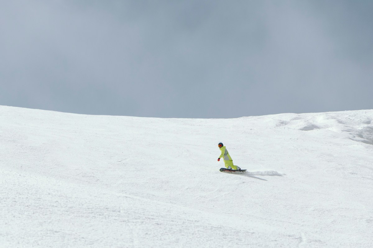 A rider uses the Burton Custom Flying V board while carving across a wide, open snowy slope
