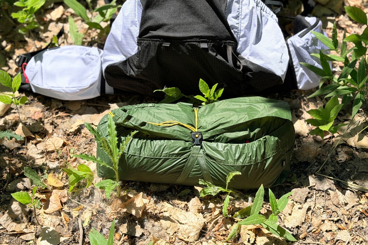 Packed green Exped Cassira Two-Person Tent sitting on dry leaves and dirt