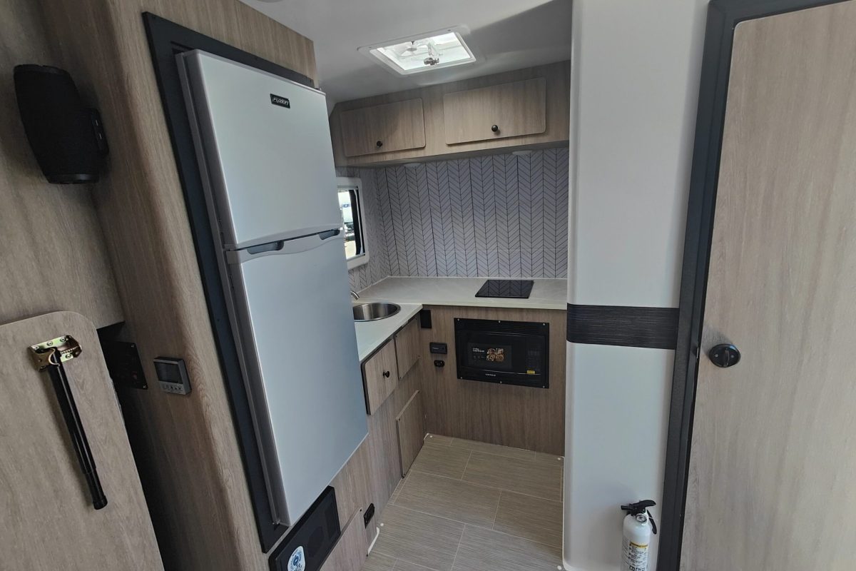 The beige and gray interior of a LIV travel trailer with refrigerator, sink, induction cooktop, and microwave.