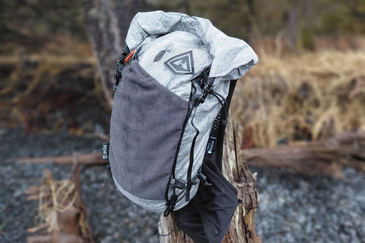Gray hiking pack with a front mesh pocket and roll-top closure on a stump