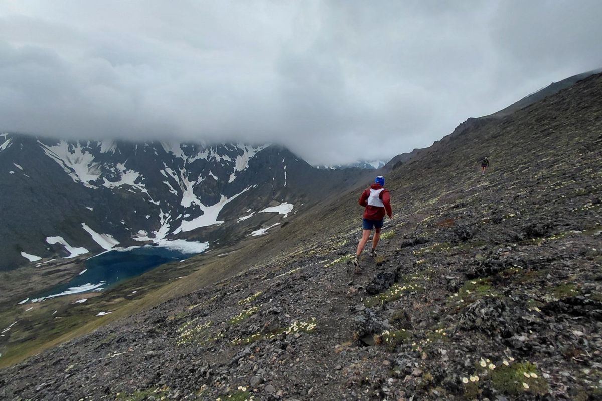 Runner wearing the vest across a steep mountainside above an alpine lake