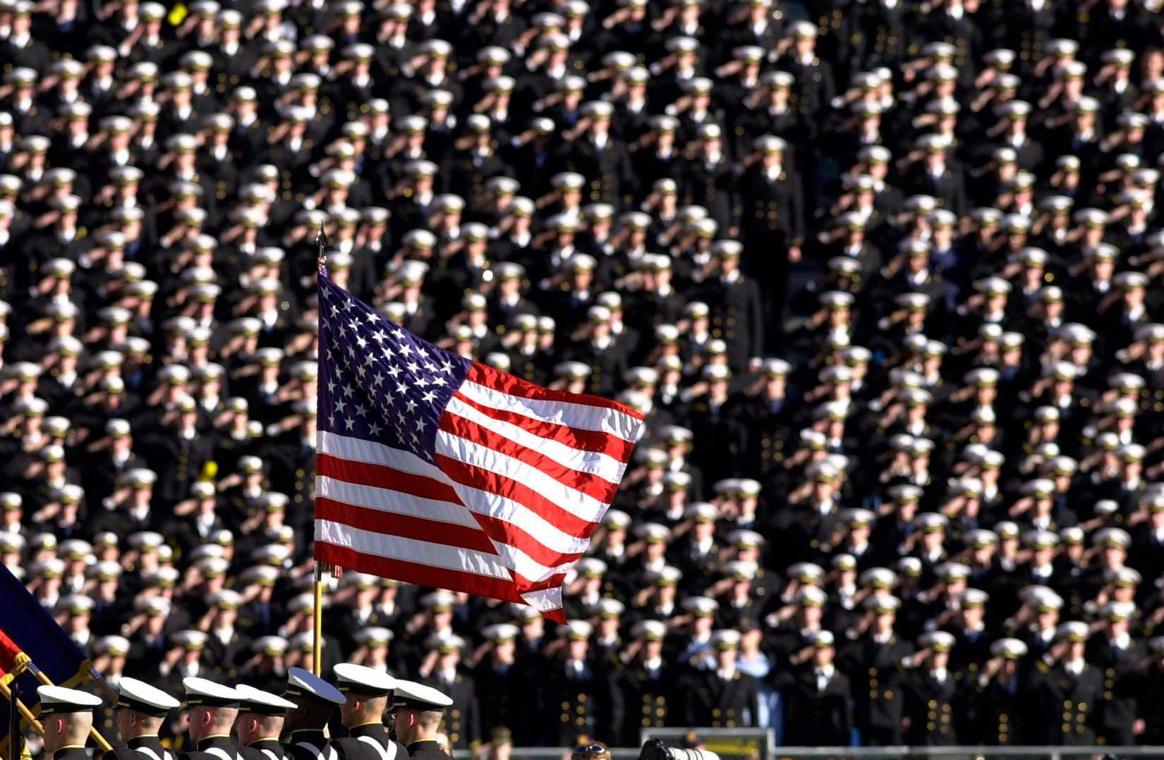 American flag flies with a background of Navy midshipmen