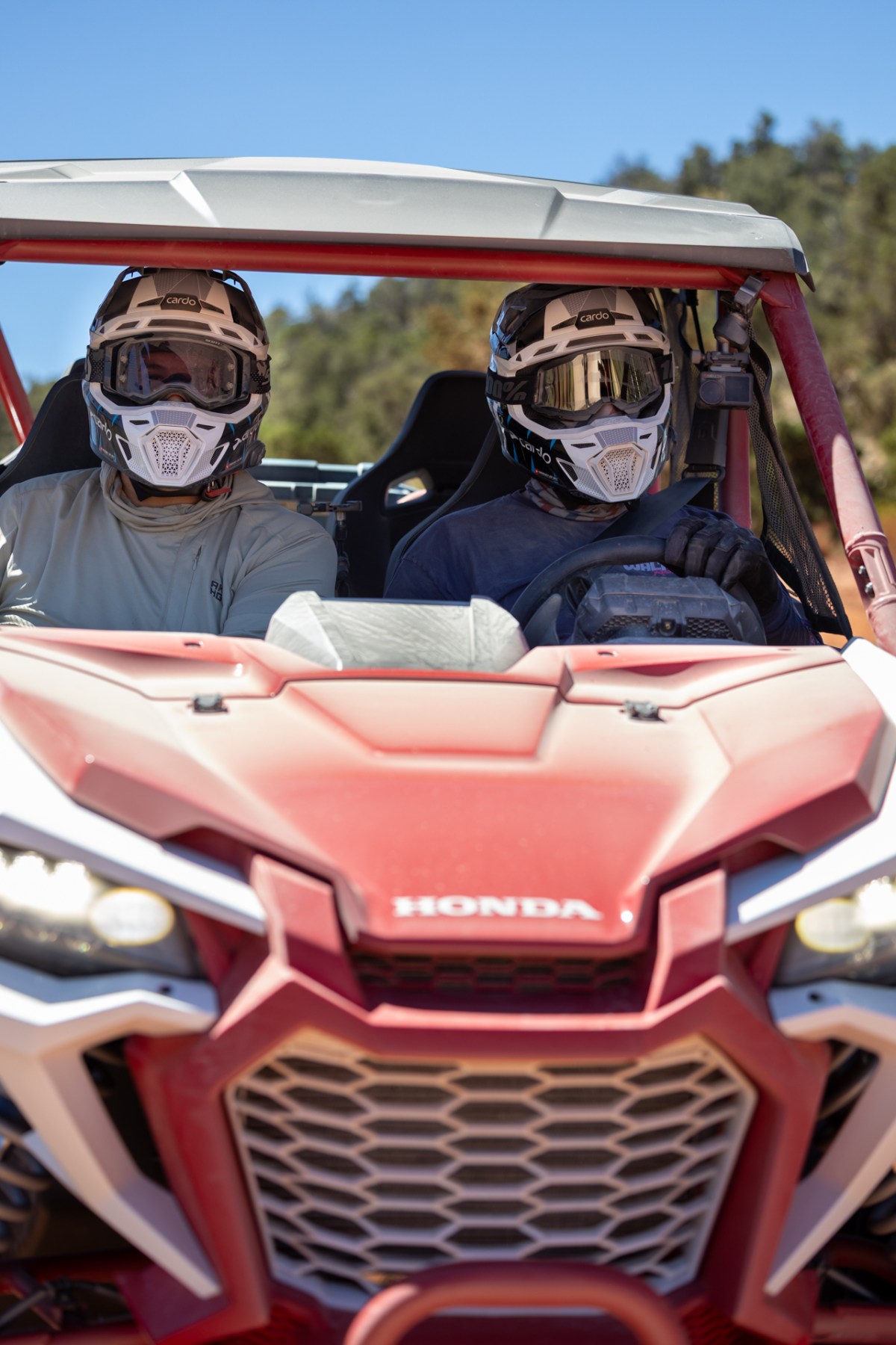 Two men in helmets sit in a red Honda side-by-side