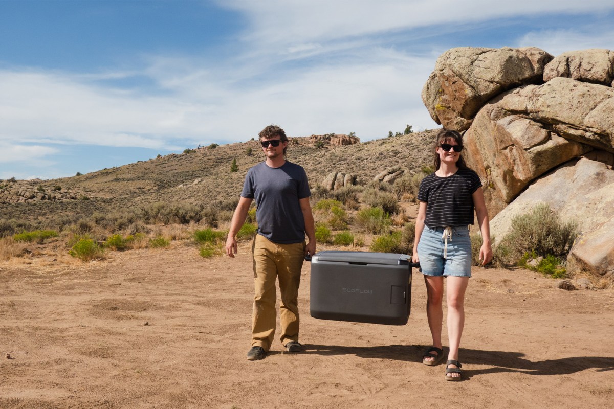 Two people carrying the EcoFlow portable fridge through a rocky campsite