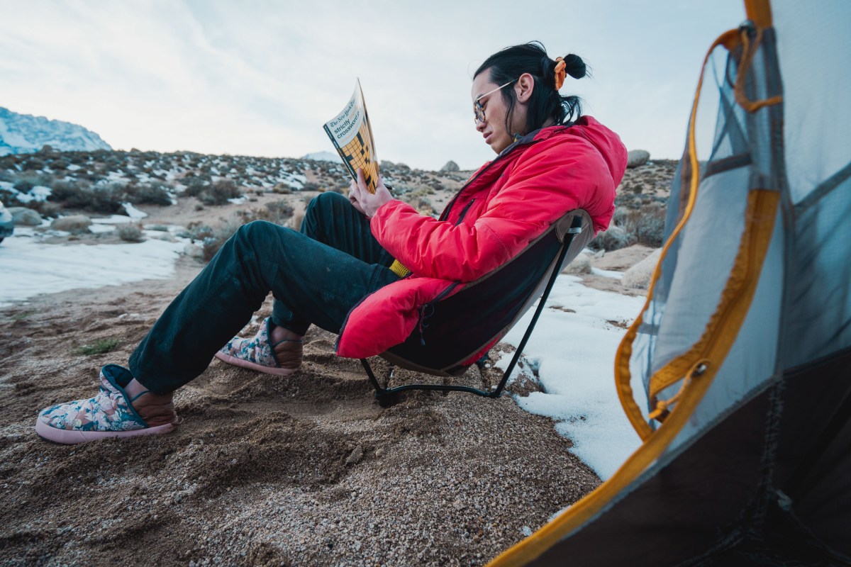 a camper sitting in the helinox ground chair while working on a crossword in camp