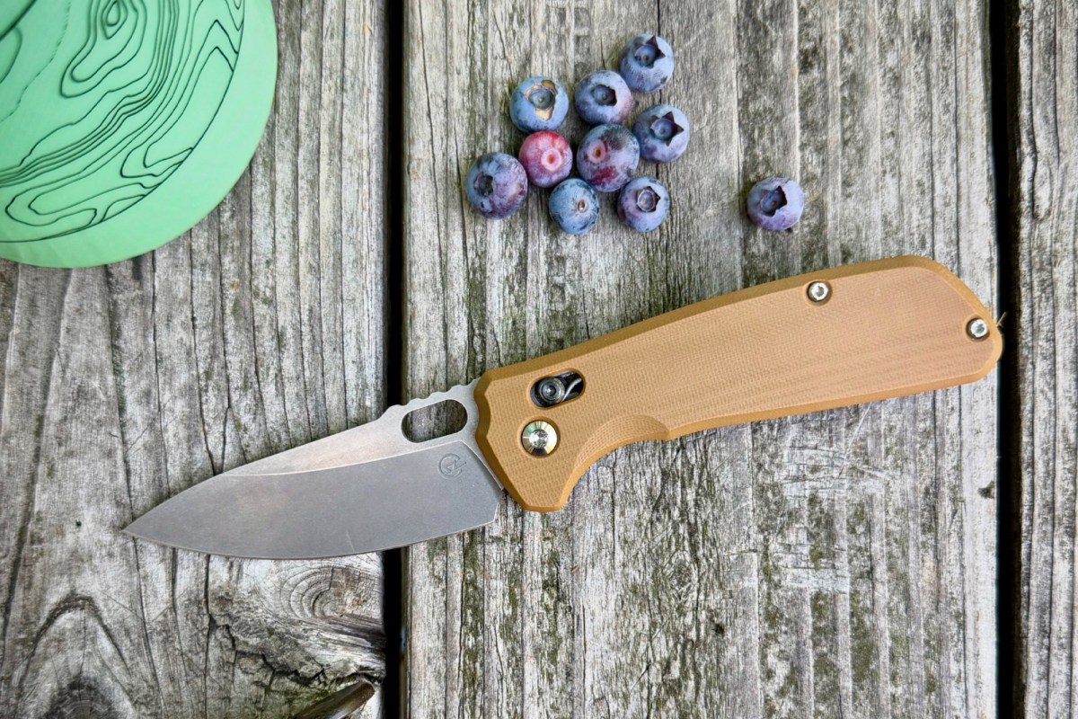 Enduro folding knife with tan handle beside blueberries on a wooden table