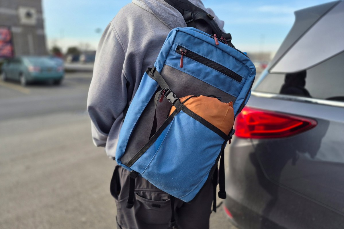 Blue Hill People Gear Commuter pack worn over one shoulder beside a car