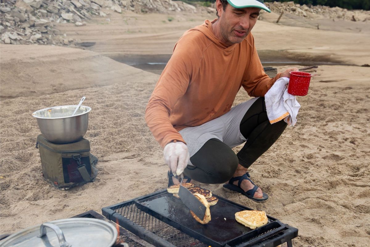 person cooks up pancakes on griddle on sand