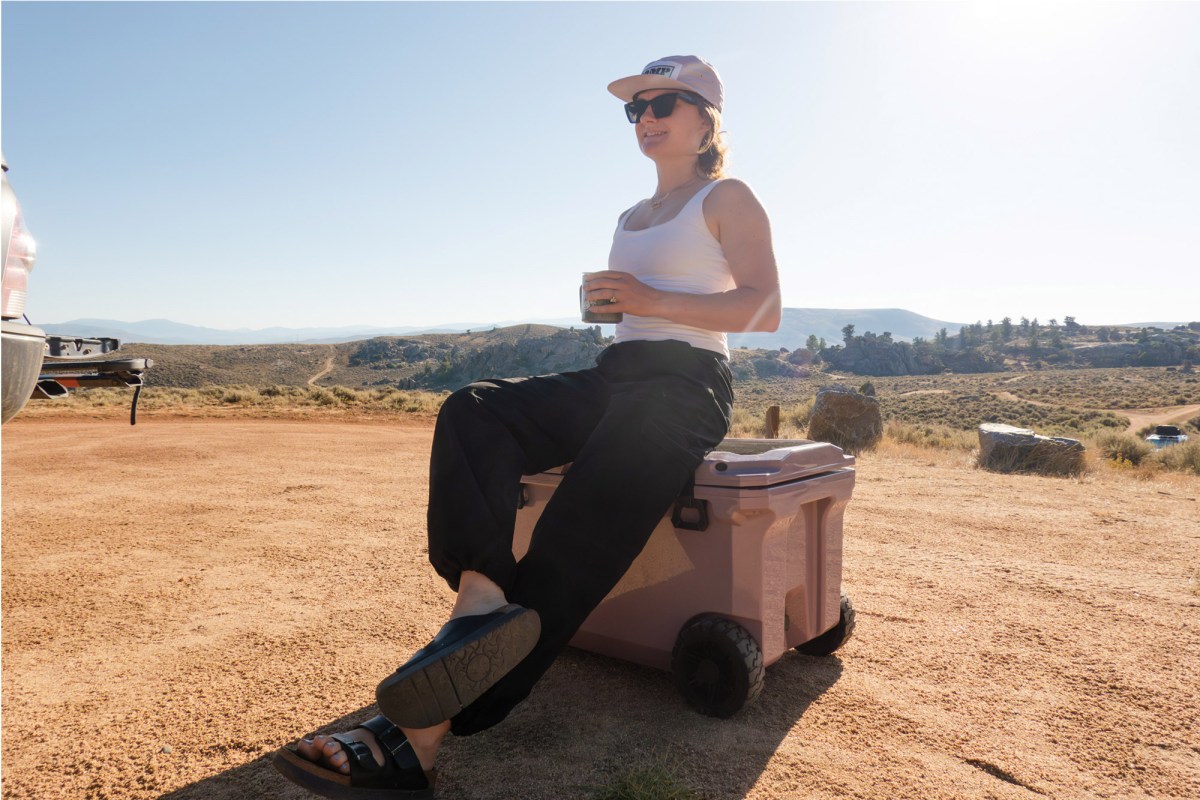 Woman relaxing on a BrüTank rolling cooler at a campsite