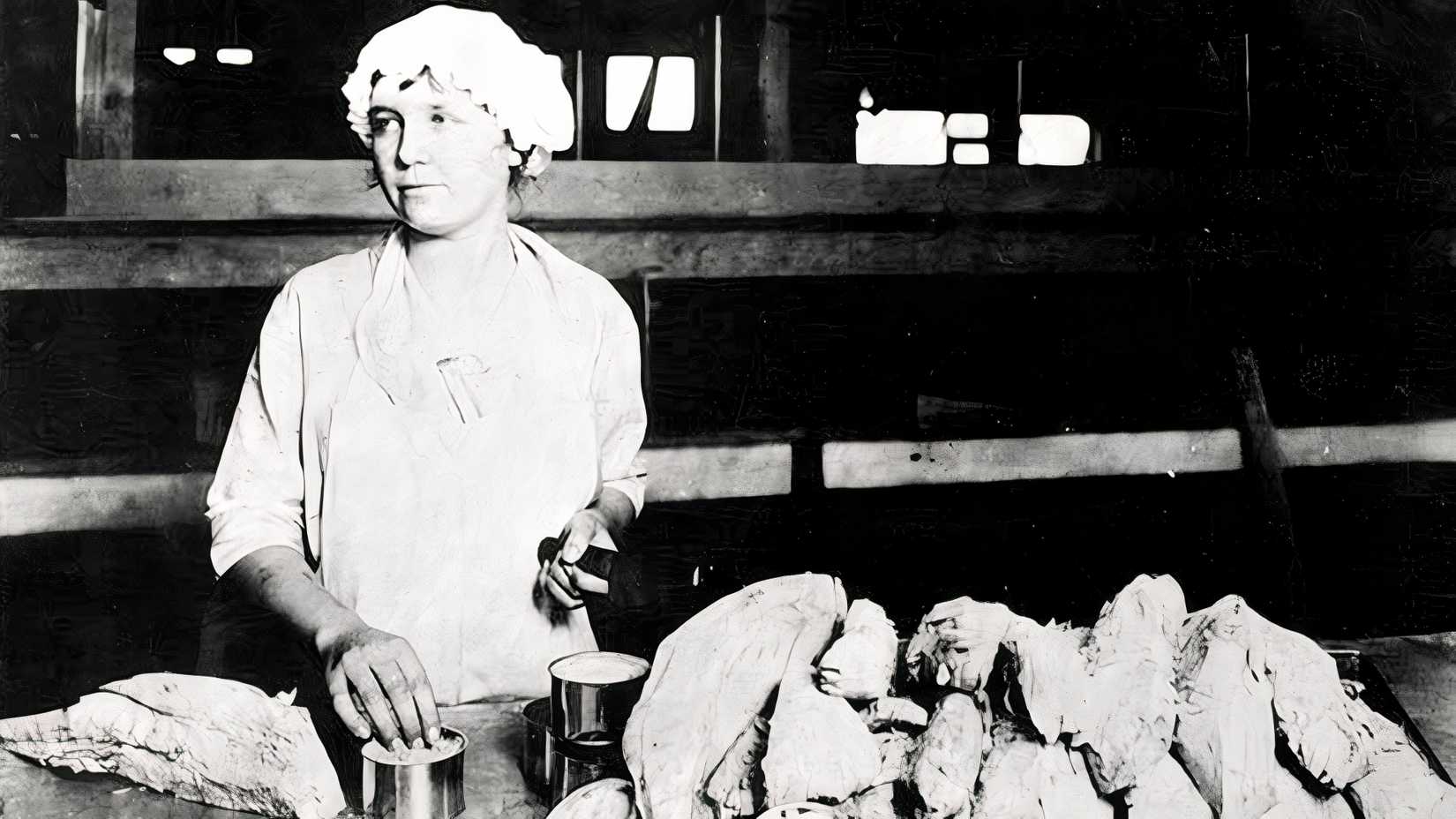 A woman fills open tuna cans beside rows of prepared fish at a California cannery in 1930.